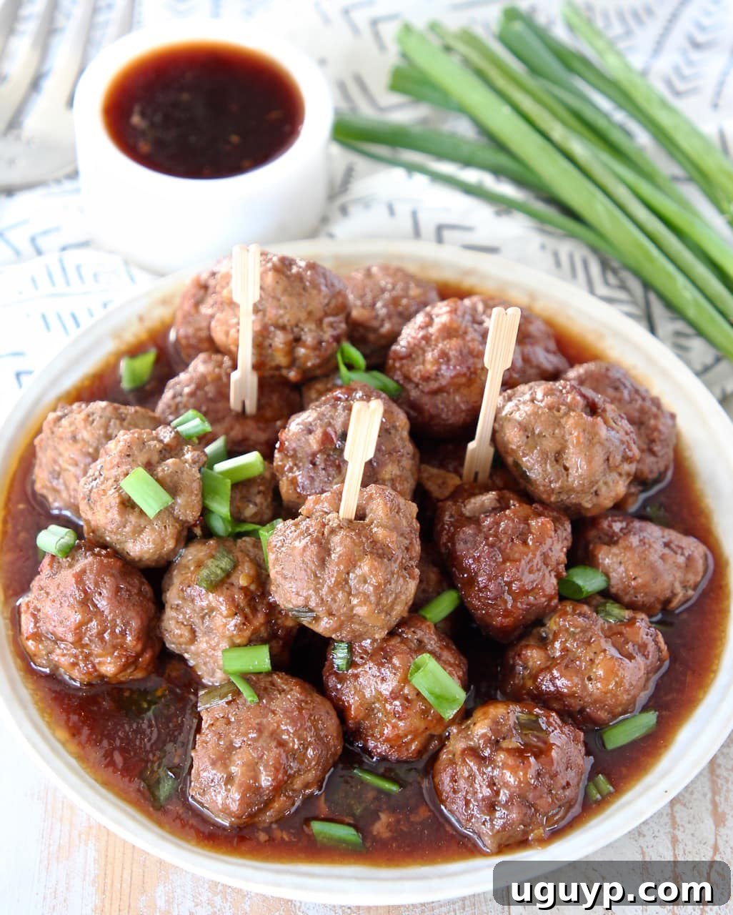 Plate of Korean BBQ meatballs with a side of Korean BBQ sauce and a garnish of green onions.