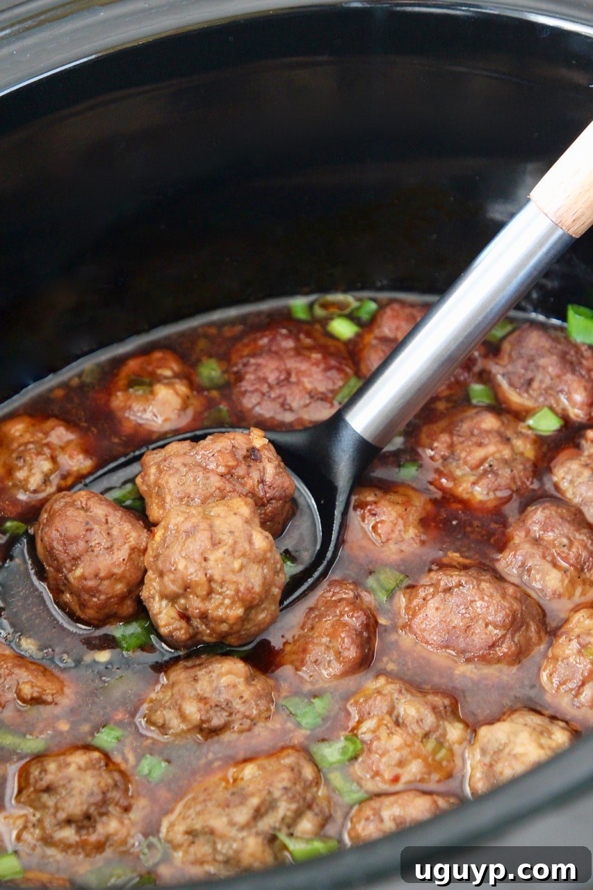 Korean BBQ meatballs being scooped from a crock pot with a large serving spoon.