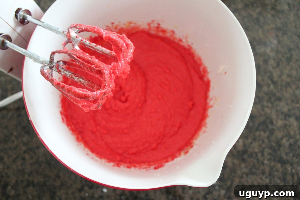 An electric mixer resting above a bowl of vibrant red velvet cookie batter.