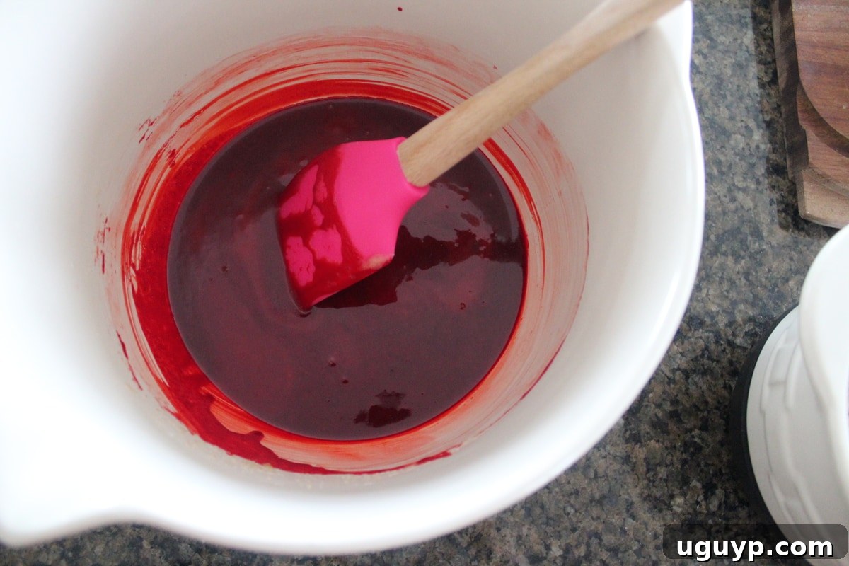 Butter, sugar, vanilla, eggs, and red food coloring mixed together in a white bowl for the brownie batter.