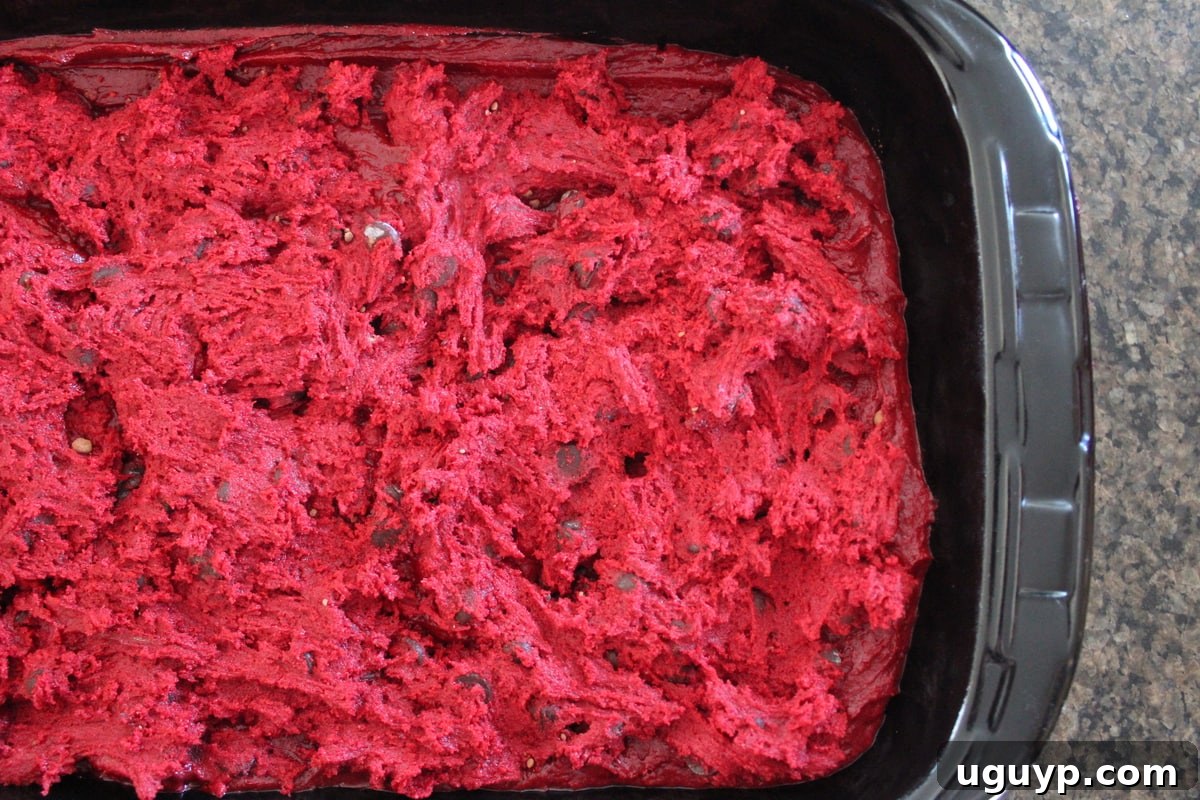 Red velvet brownie batter topped with dollops of red velvet cookie dough in a baking dish, ready for baking.