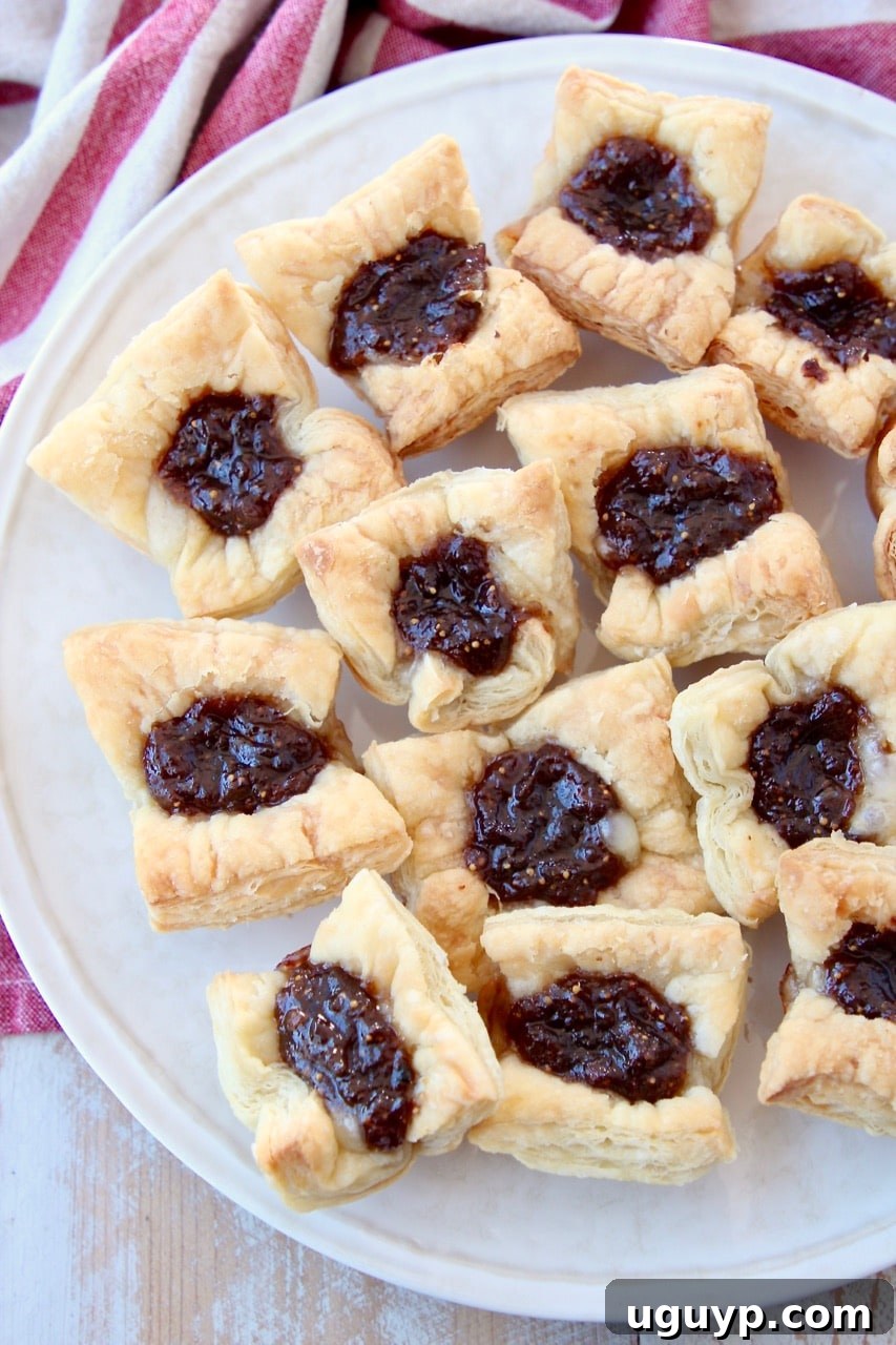 Golden baked puff pastry bites, generously filled with melted brie and a dollop of sweet fig jam, beautifully arranged on a serving plate.