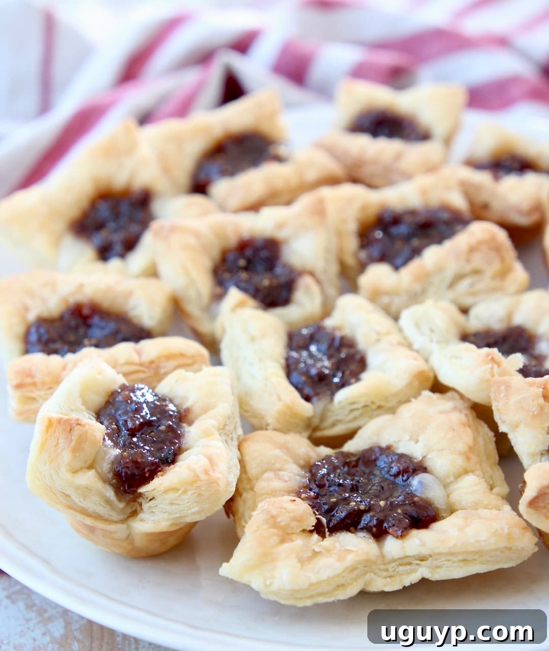 Close-up of a plate with several baked puff pastry bites, showing the gooey brie and vibrant fig jam filling.
