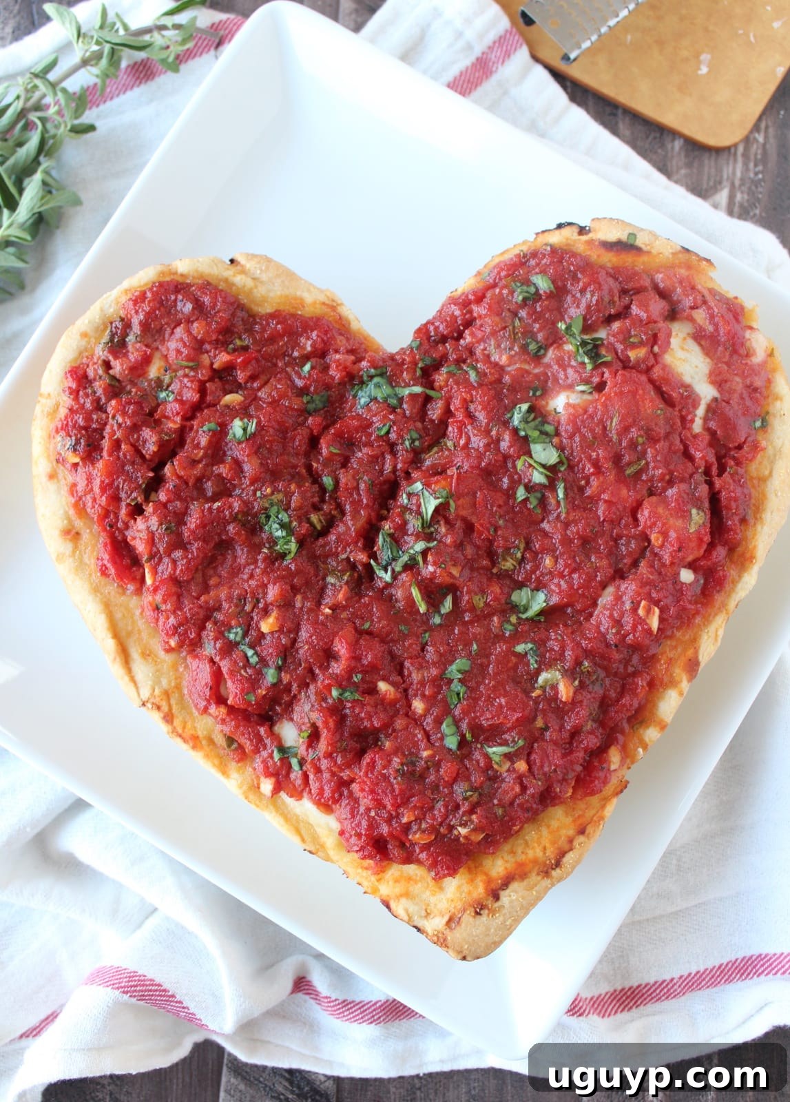 A heart shaped deep dish pizza on a white plate with a slice removed.