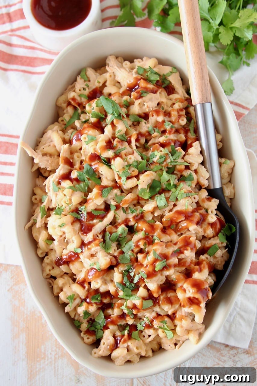 Mac and cheese in large oval baking dish, topped with bbq sauce, with a large serving spoon in the dish