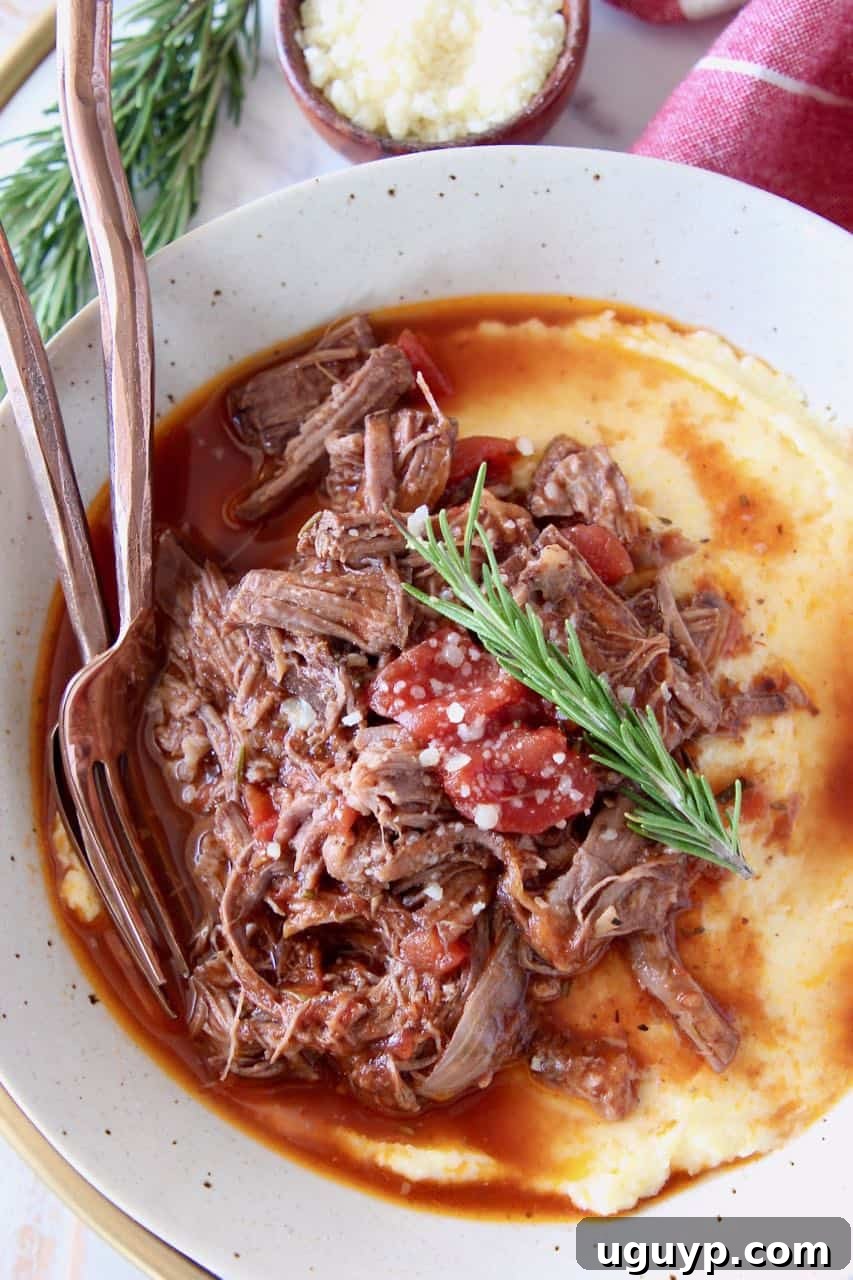 Shredded beef ragu sauce served over creamy polenta in a white bowl, garnished with herbs