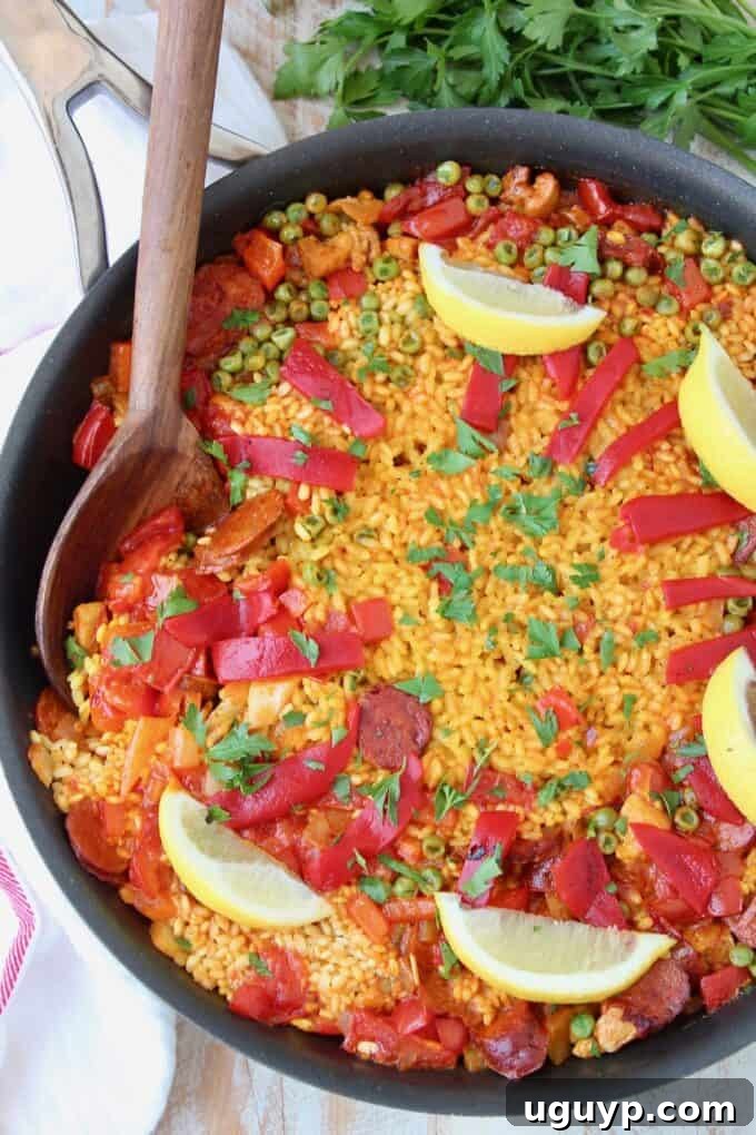 A large skillet of Spanish Chicken and Chorizo Paella, perfectly cooked and garnished, with a wooden serving spoon ready to dish out portions.