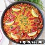 Overhead view of a cooked Spanish paella in a skillet, garnished with fresh lemon wedges, ready to be served.