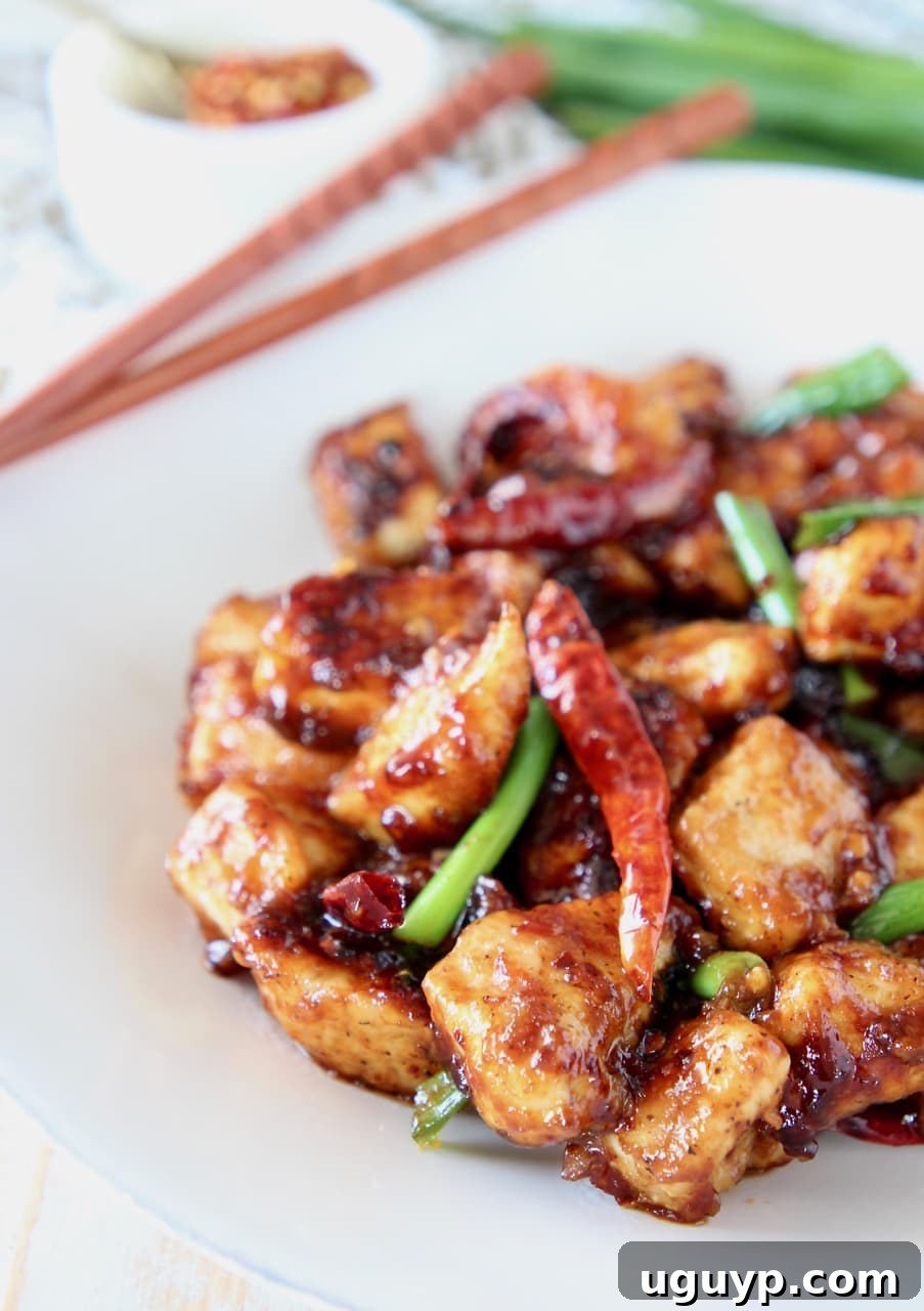 Gluten-free General Tso Chicken with red chili peppers and green onions on a white plate with wood chopsticks, ready to be enjoyed.