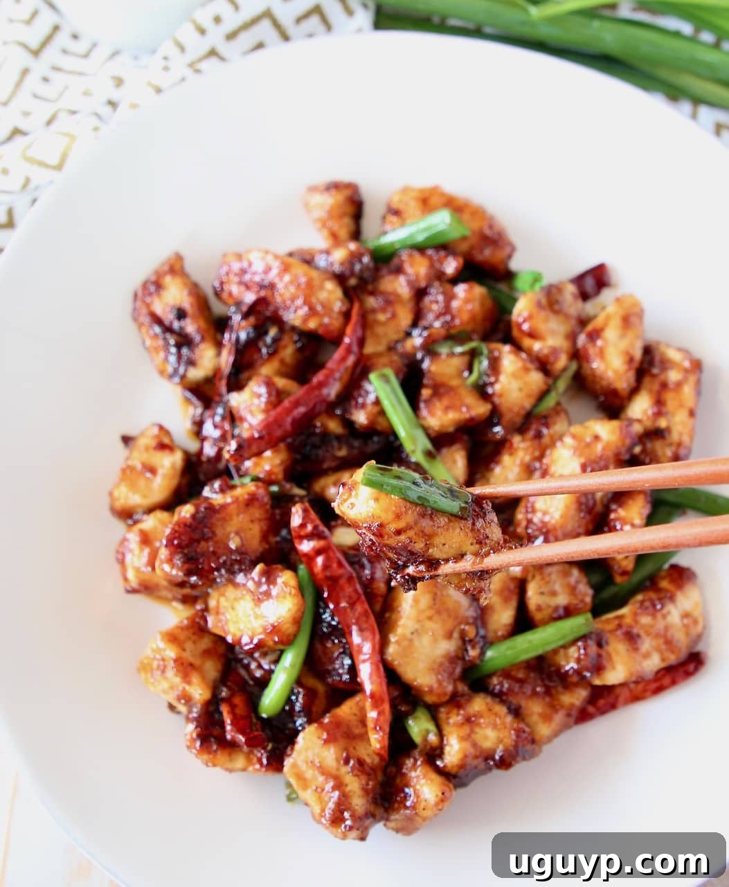 Gluten-free General Tso Chicken on a white plate with chopsticks picking up a piece of chicken, highlighting its delicious texture.
