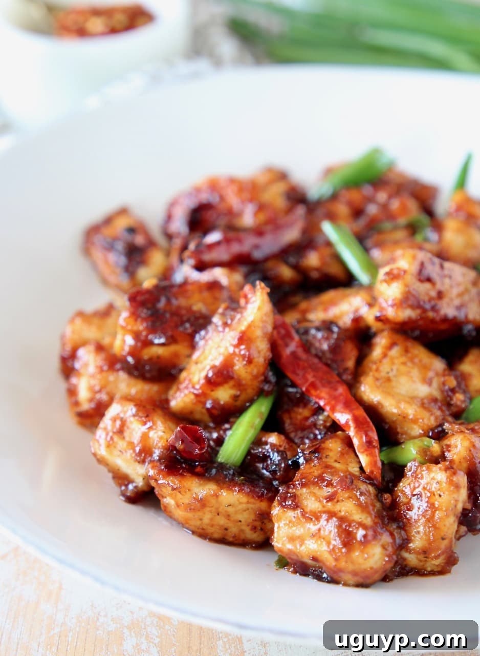 Gluten-free General Tso Chicken on a plate with red chilies and scallions, garnished beautifully.