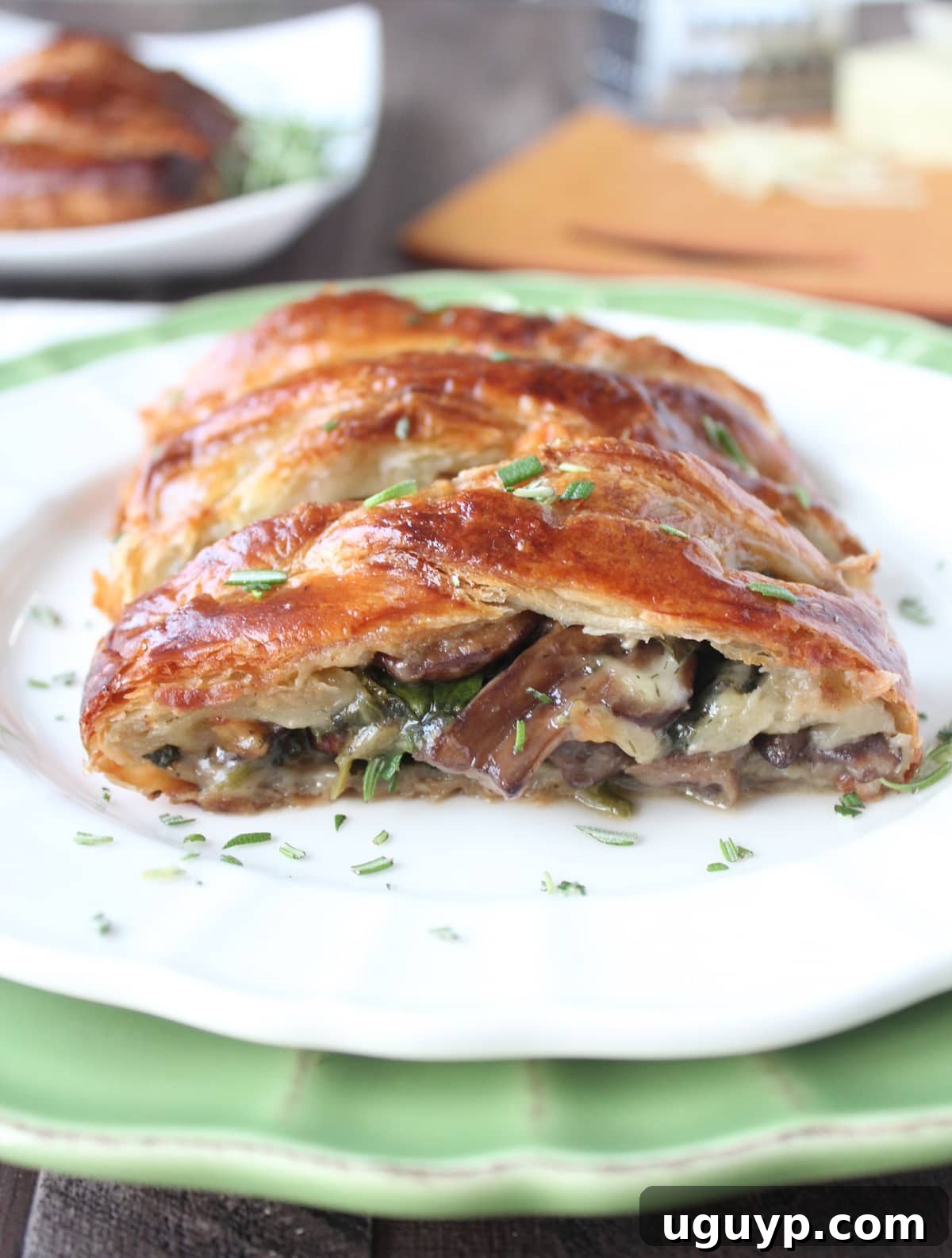 Golden brown puff pastry filled with cheese, mushrooms, and spinach, garnished with fresh rosemary on a white plate, ready to be served.