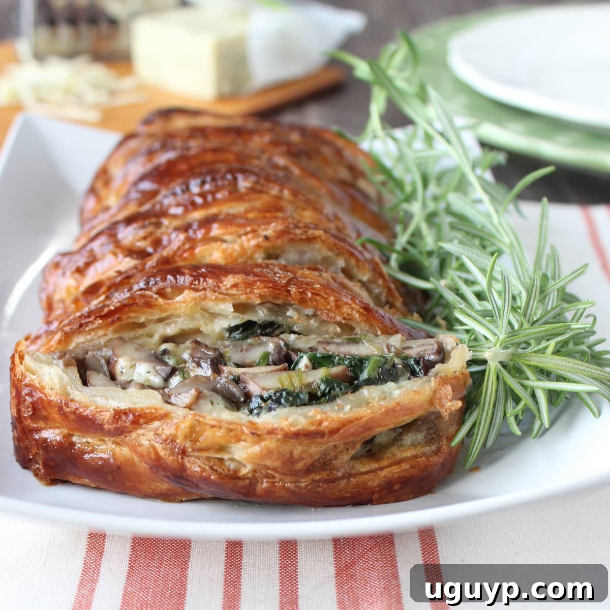 A beautifully baked, braided puff pastry on a white plate, garnished with fresh rosemary sprigs, highlighting its golden crust.