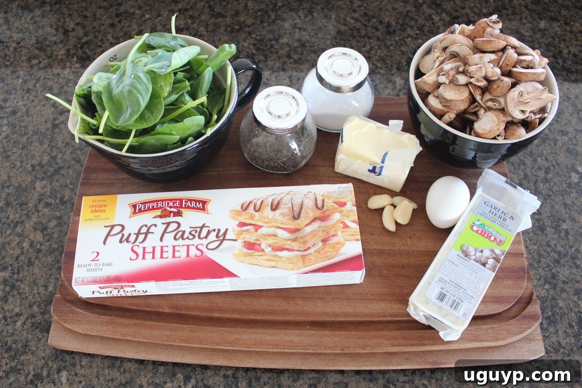 Fresh ingredients for mushroom spinach puff pastry laid out on a rustic wood cutting board: butter, baby bella mushrooms, garlic, baby spinach, shredded cheddar cheese, and a sheet of puff pastry dough.