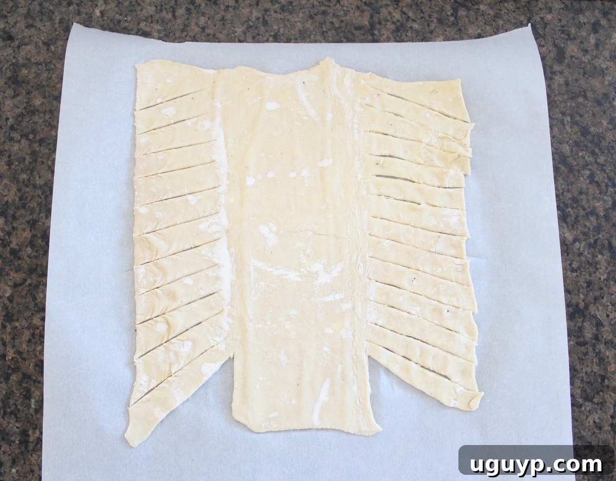 A sheet of puff pastry dough on parchment paper, with diagonal slices made along the sides for braiding.