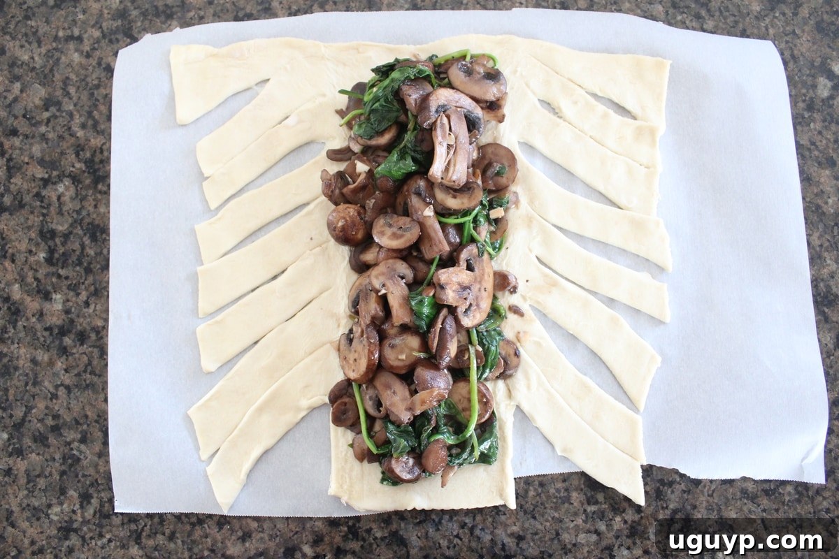 Sautéed sliced mushrooms and spinach placed neatly on top of a sheet of puff pastry dough.