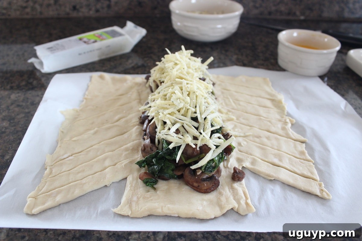 Shredded cheddar cheese layered over the spinach and mushrooms on a sheet of puff pastry dough.