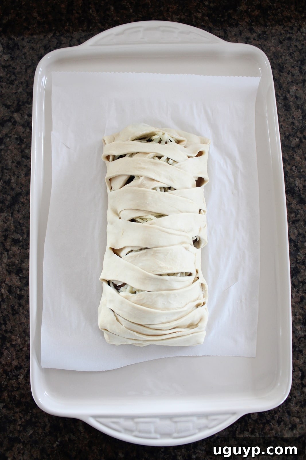A braided puff pastry dough on a parchment-lined baking sheet, prepared for baking.