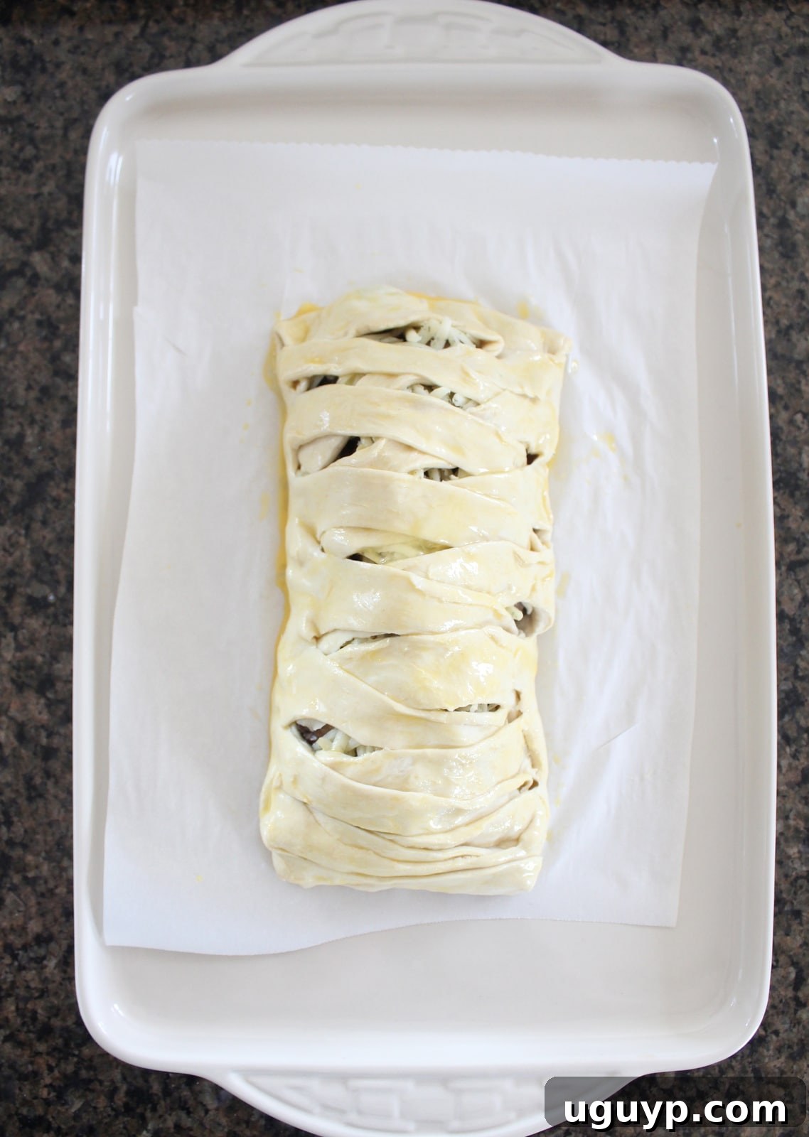 Egg wash being brushed over the braided puff pastry dough, ready for baking.