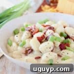 Gnocchi in cream sauce in bowl topped with bacon pieces and diced green onions