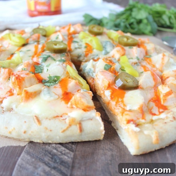 A perfect slice of Buffalo Chicken Dip Pizza being removed from the whole pie, showing the gooey cheese and chicken.