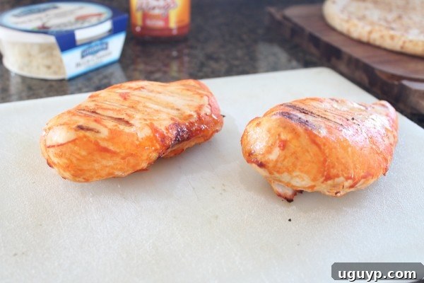 Perfectly cooked buffalo chicken breasts resting on a white surface, ready to be diced.