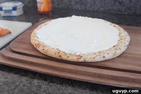 A pre-cooked pizza crust coated with a creamy cheese sauce, ready for toppings.