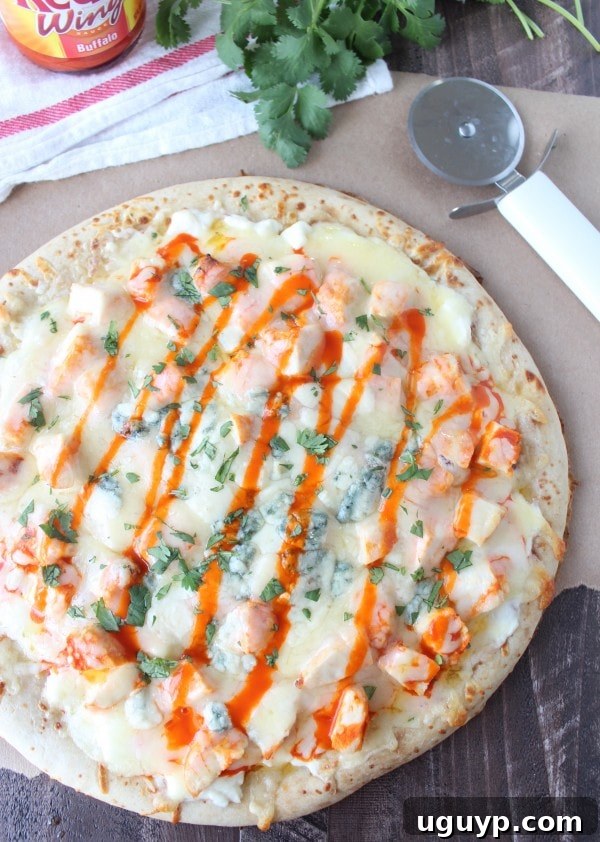 A whole Buffalo Chicken Dip Pizza displayed on a wooden surface next to a pizza cutter, ready to be enjoyed.