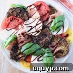 A vibrant Caprese salad with sliced tomatoes, mozzarella, crispy eggplant, prosciutto, fresh basil, and balsamic glaze drizzle on a white plate.