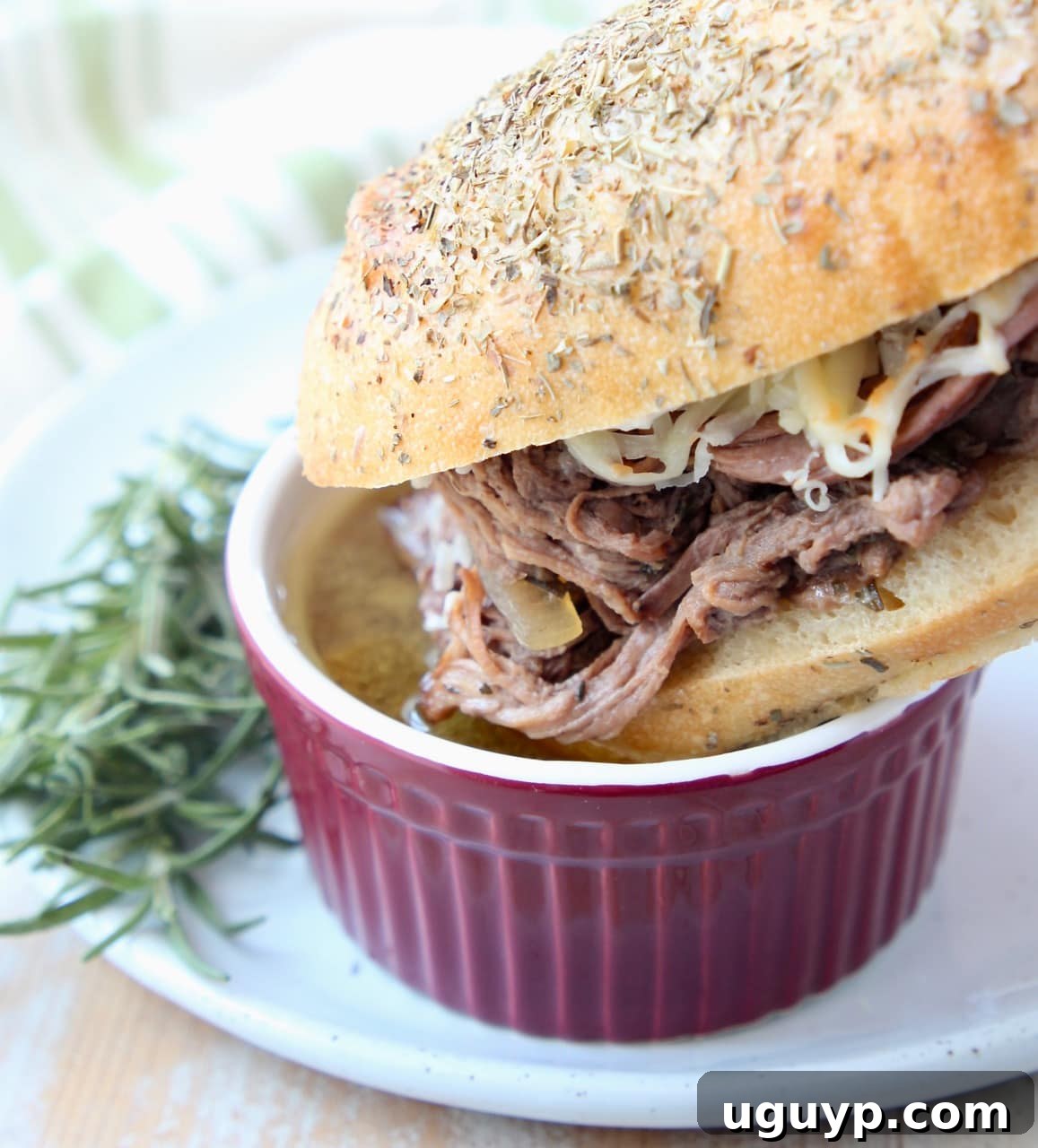 A French Dip Sandwich being dipped into a small bowl of savory au jus, highlighting the rich broth.