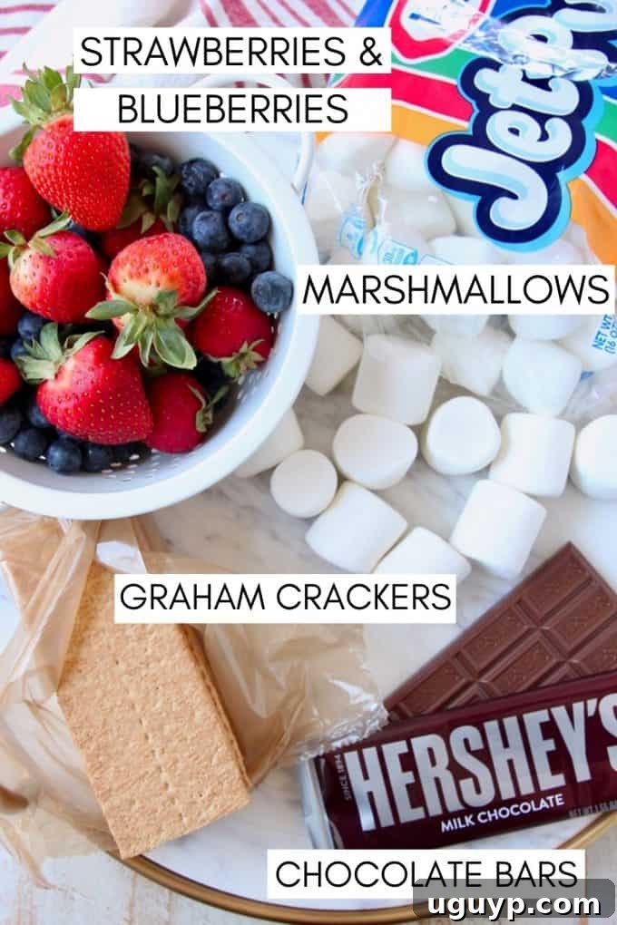 Ingredients for berry s'mores laid out on a table: graham crackers, marshmallows, chocolate bars, fresh strawberries, and blueberries.