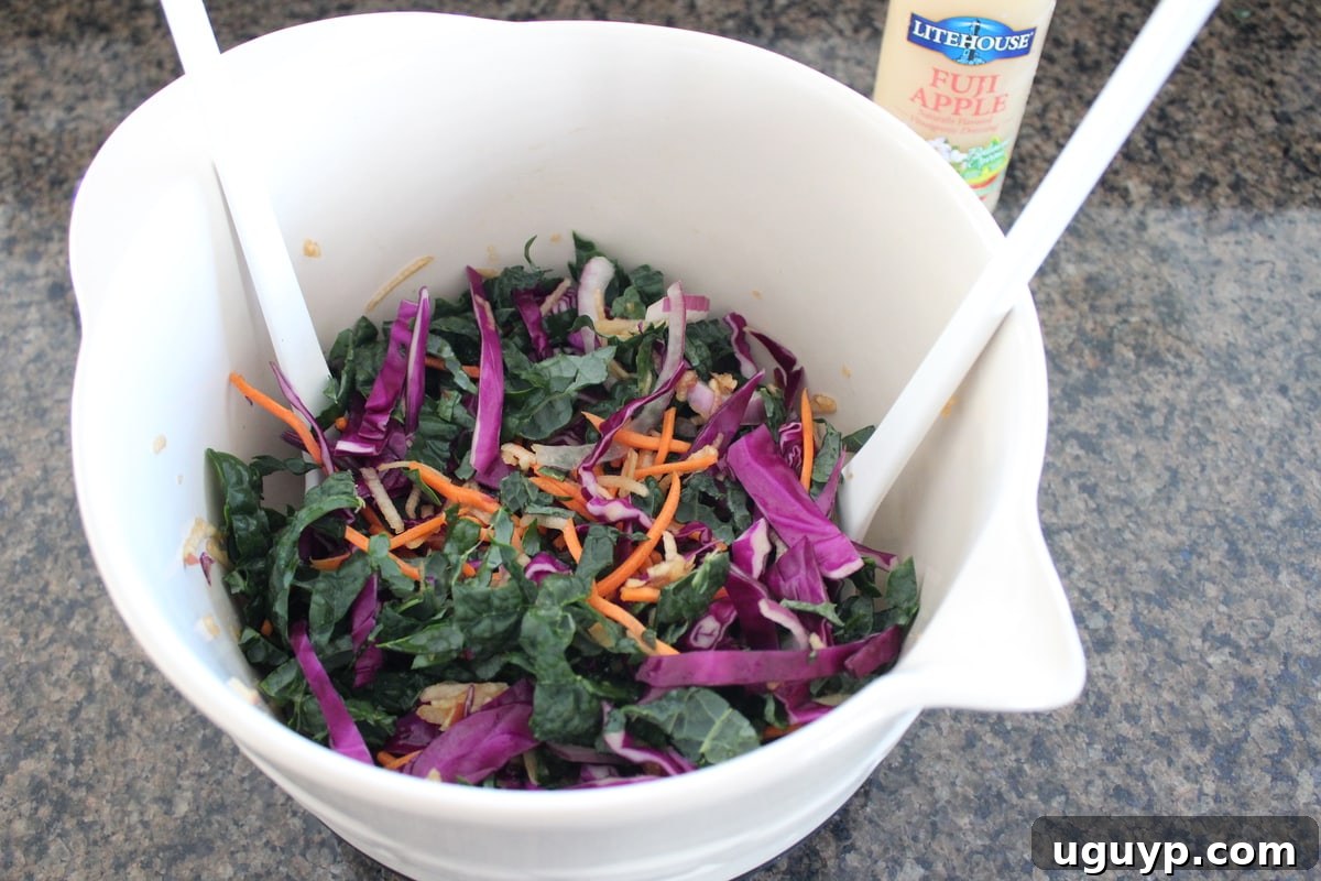 All the freshly prepared ingredients for Kale Apple Slaw are shown in a large mixing bowl, tossed together with dressing, illustrating the mixing process before serving.