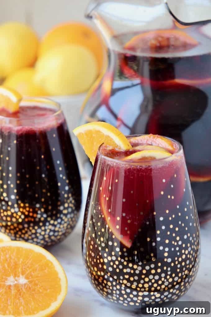 Red sangria in glasses and a pitcher, garnished with fresh oranges, ready for serving.