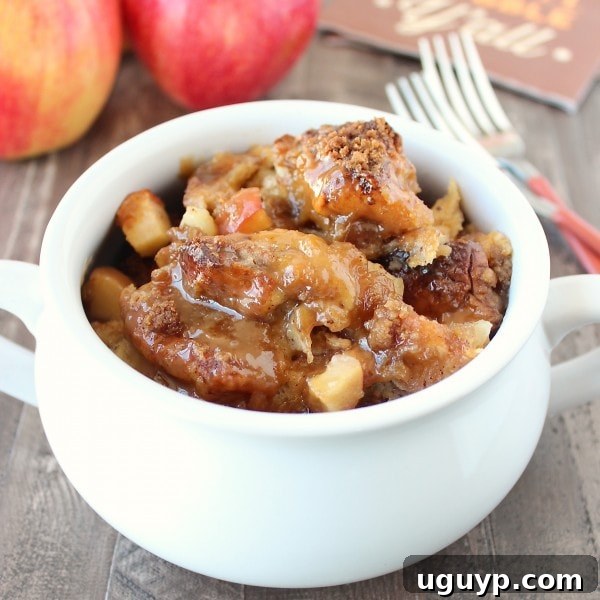 Close-up of baked caramel apple bread pudding in a white serving bowl, showing the soft interior and caramel drizzle.