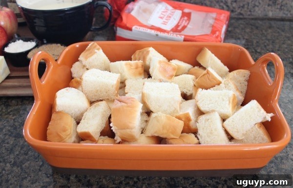 Cubed Hawaiian rolls arranged neatly in an orange ceramic baking dish, ready for the custard mixture.