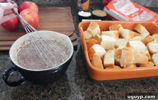 A whisk blending milk, eggs, and cinnamon in a clear glass bowl, forming the creamy custard base for the bread pudding.