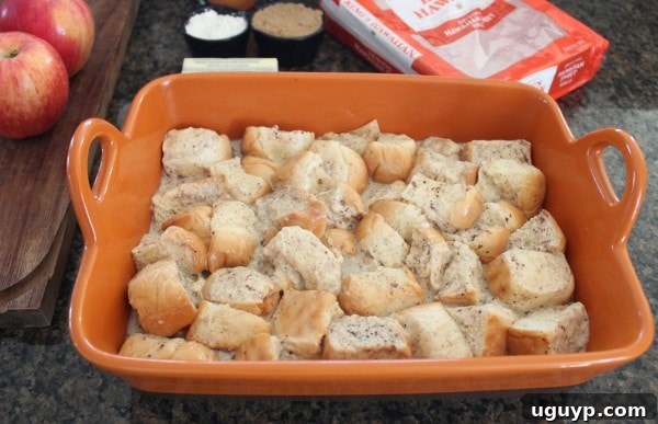 Unbaked bread pudding mixture, with Hawaiian roll cubes soaking in the custard in an orange baking dish.