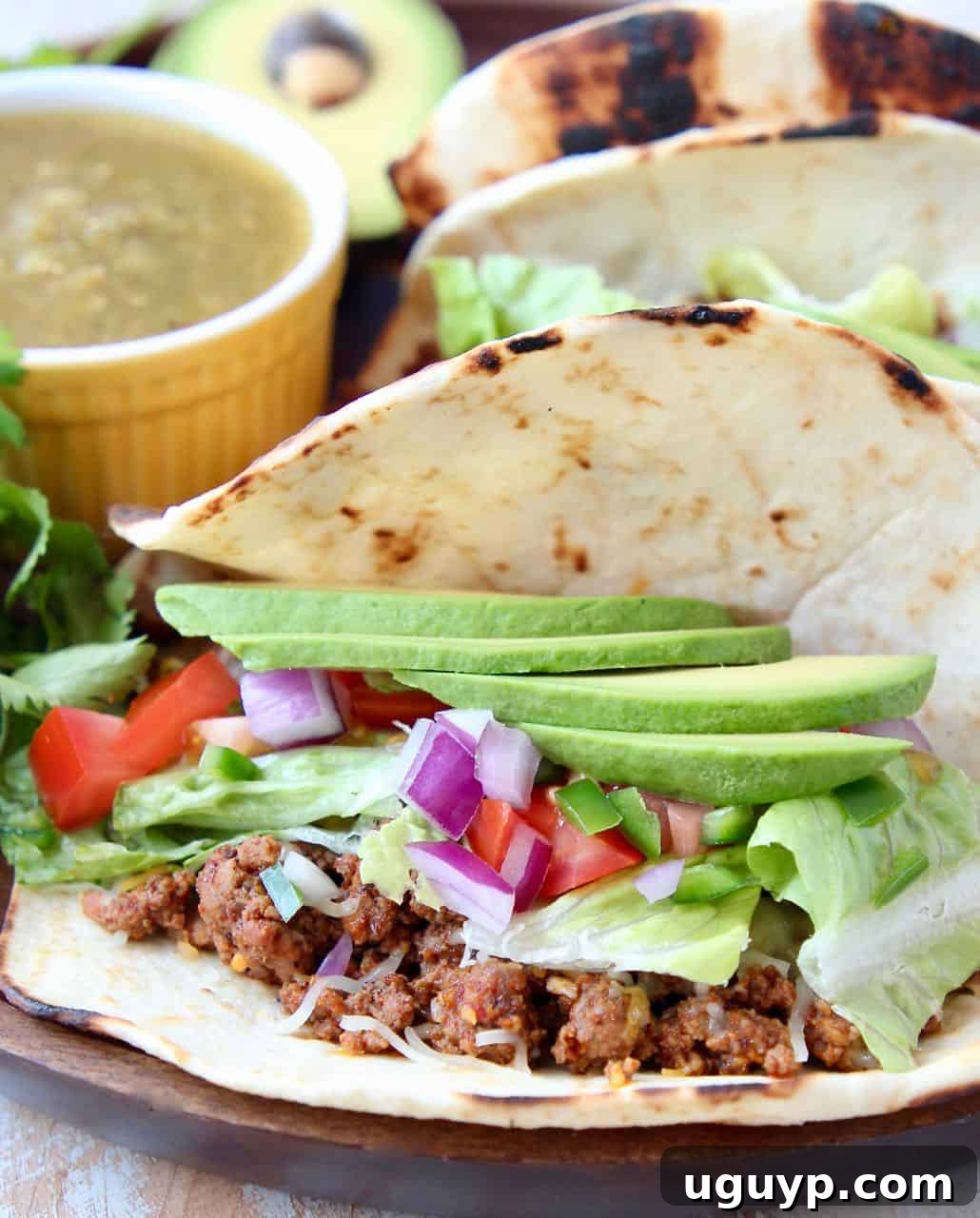 Ground beef taco in flour tortilla topped with sliced avocado