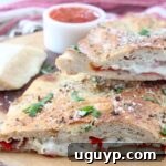 A delicious homemade calzone cut in half on a wood serving tray, showcasing its melted cheesy interior with pepperoni and vegetables.
