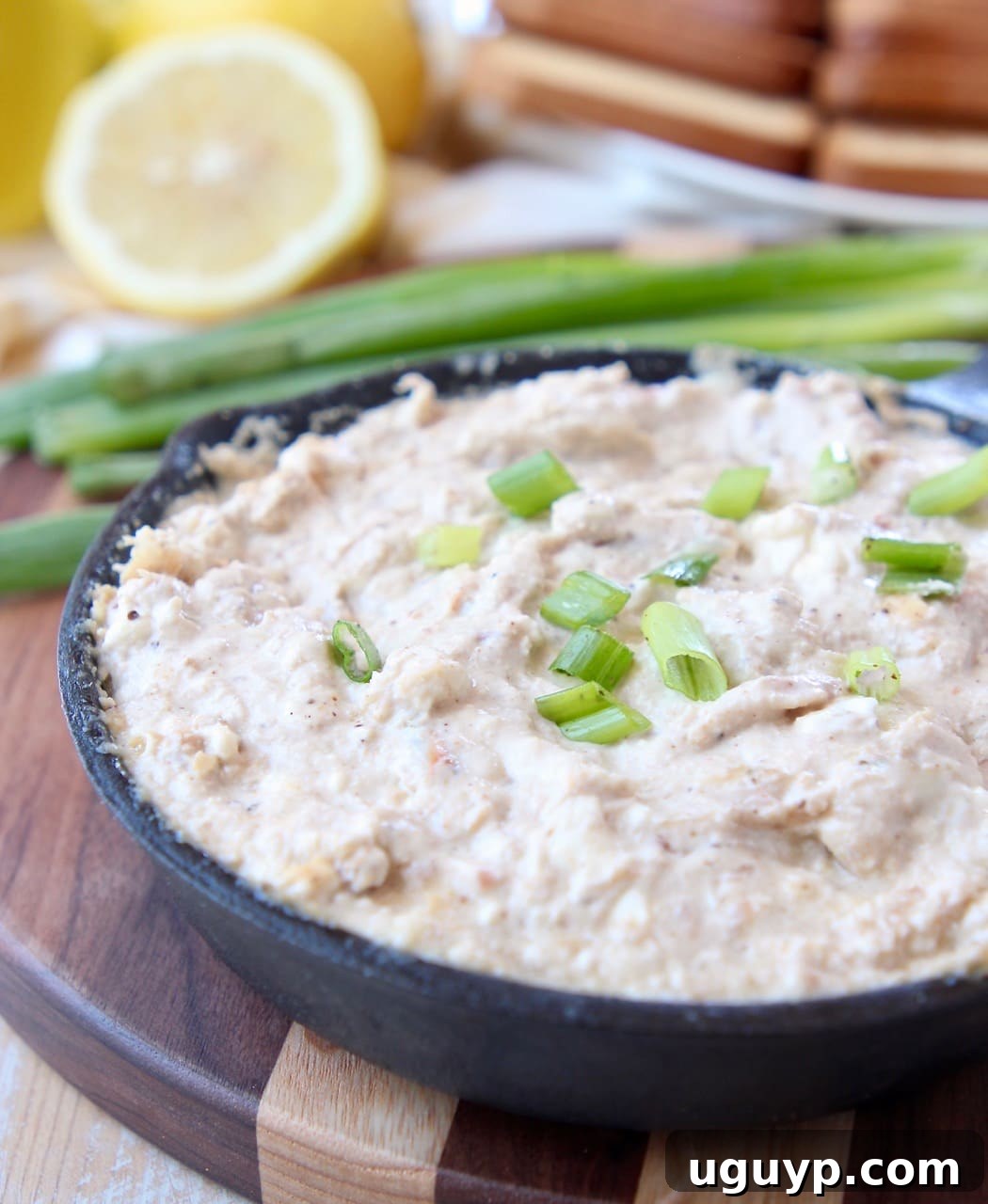 Hot crab dip in cast iron skillet, sitting on wood cutting board, garnished with fresh herbs