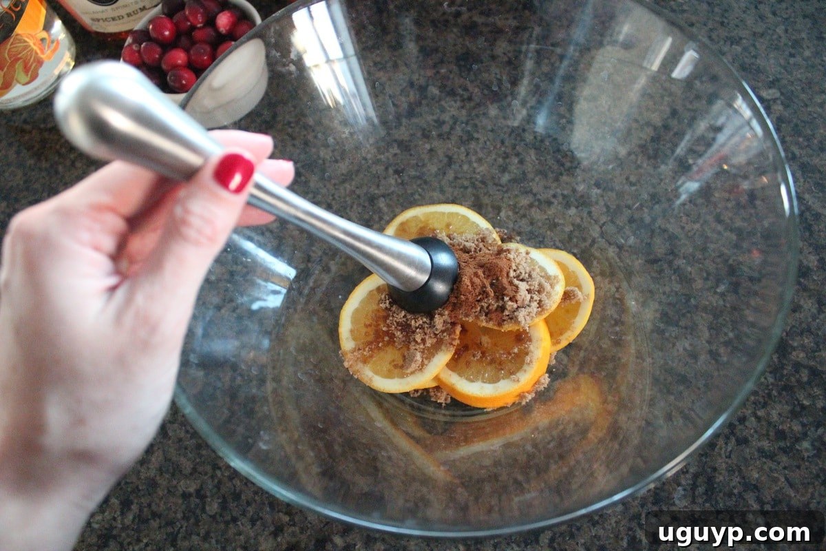 Preparing Cranberry Apple Sangria: adding liquids and fruits to a pitcher with muddled oranges