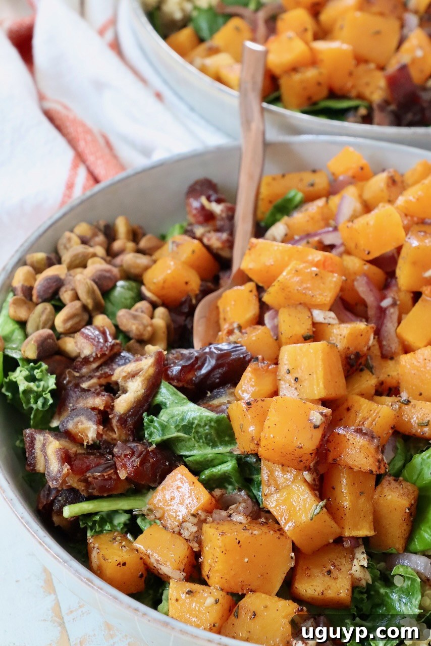 A beautifully arranged roasted butternut squash salad, featuring vibrant greens, tender squash cubes, and colorful toppings in a rustic bowl.