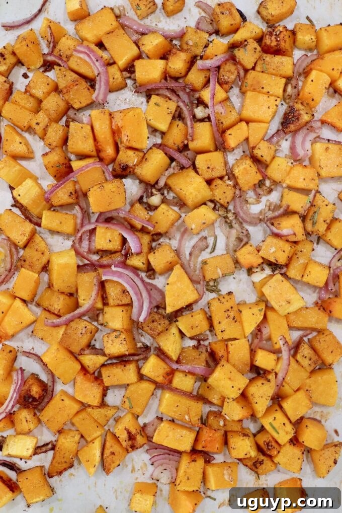 Perfectly roasted butternut squash cubes, caramelized red onions, and golden garlic cloves on a baking sheet after being cooked to tender perfection.