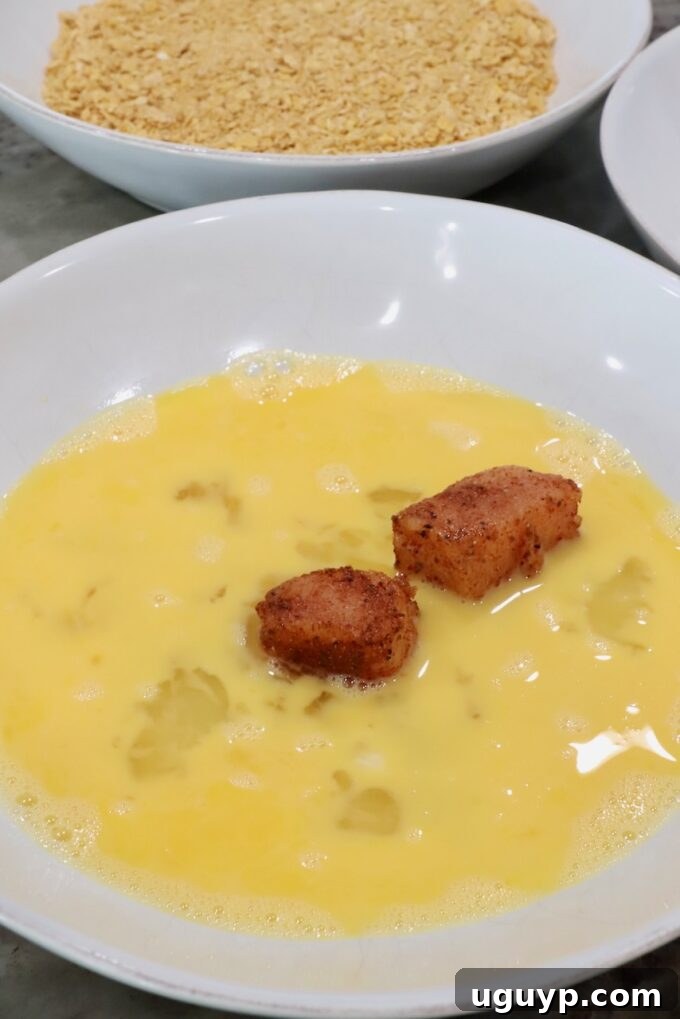 Seasoned raw pieces of chicken in a bowl of whisked eggs