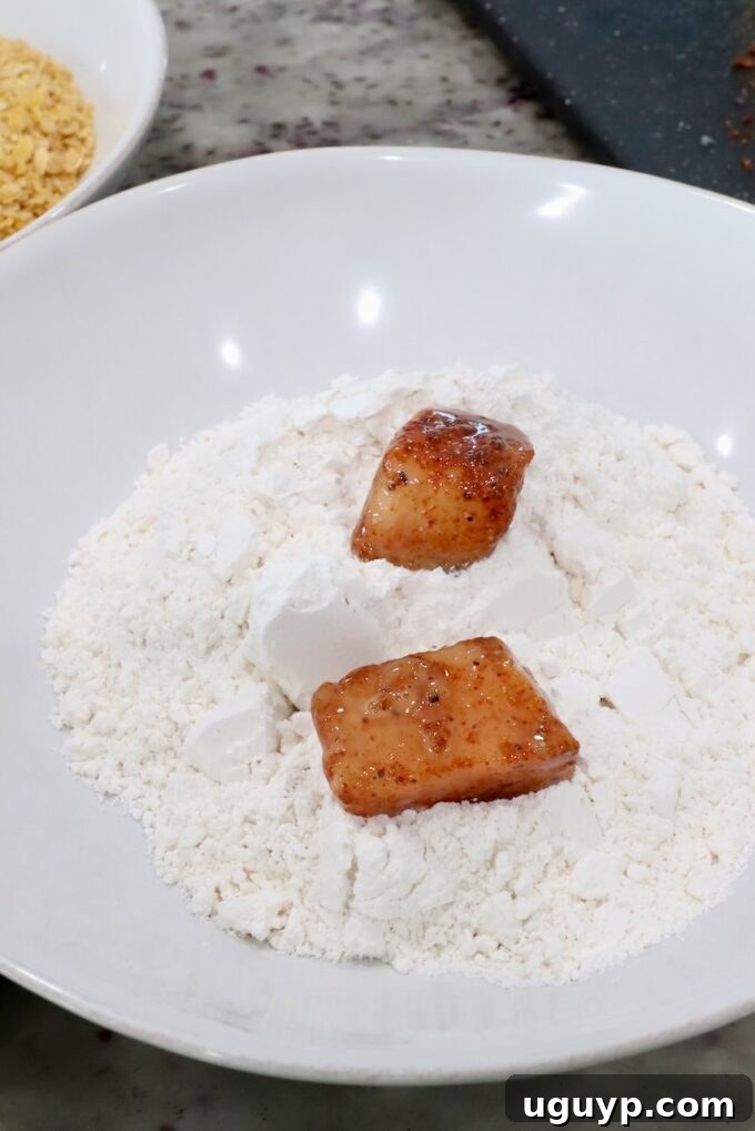 Seasoned raw pieces of chicken in a bowl of flour