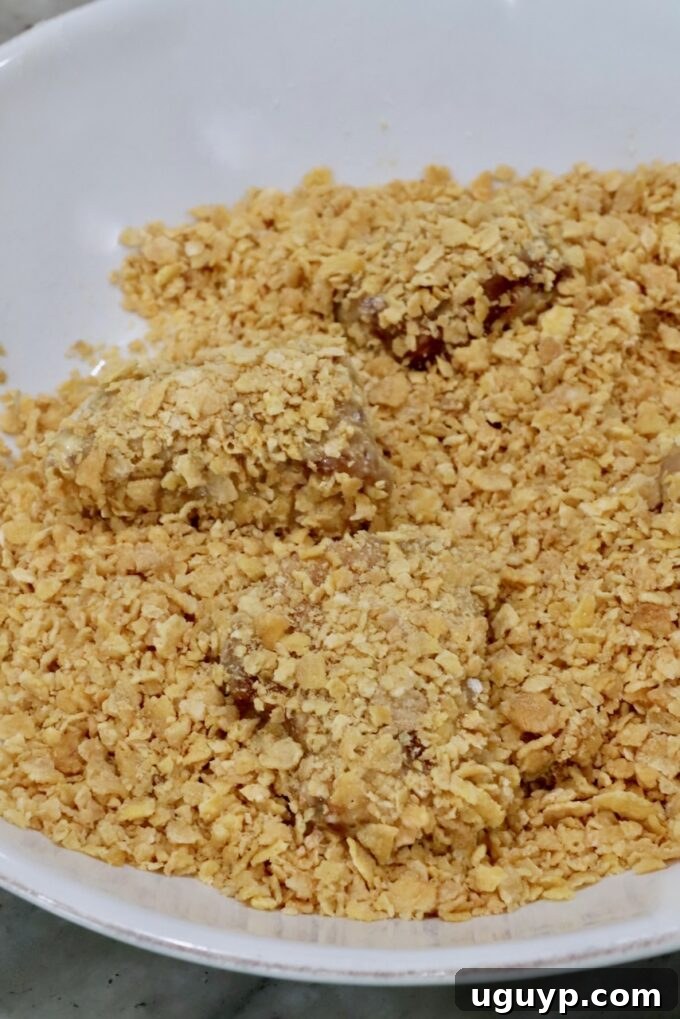 Breaded pieces of chicken in a bowl of crushed corn flakes