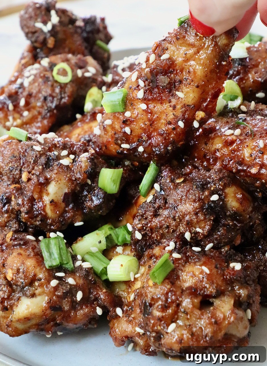 Hand grabbing a crispy General Tso chicken wing from a pile on a plate, garnished with green onions and sesame seeds
