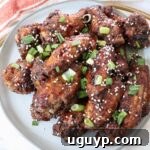Cooked General Tso chicken wings tossed in sauce and piled up on a plate with diced green onions and sesame seeds