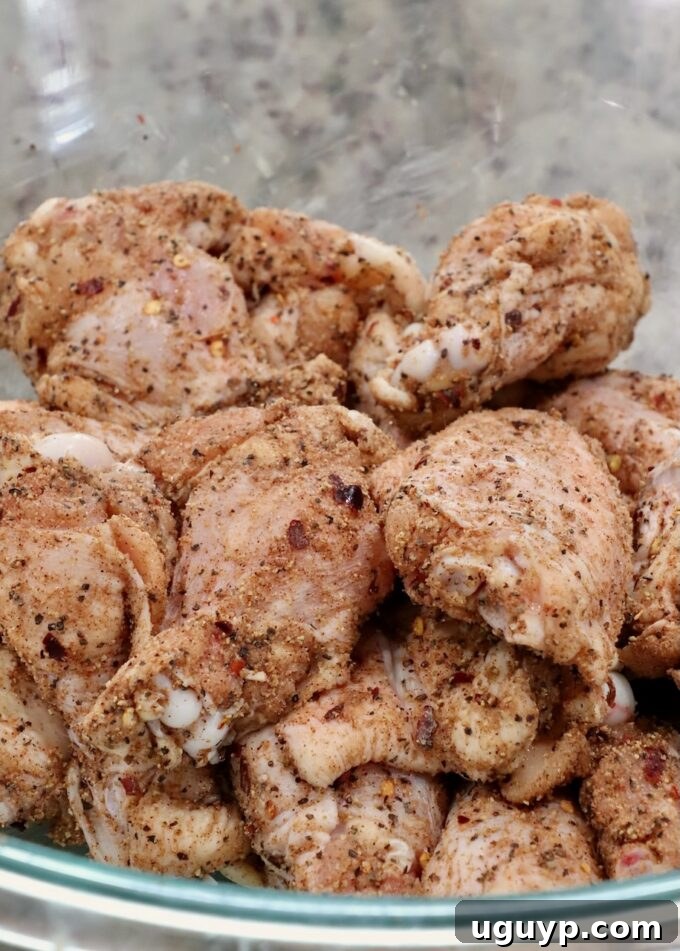 Seasoned raw chicken wings in a glass bowl, ready for cooking