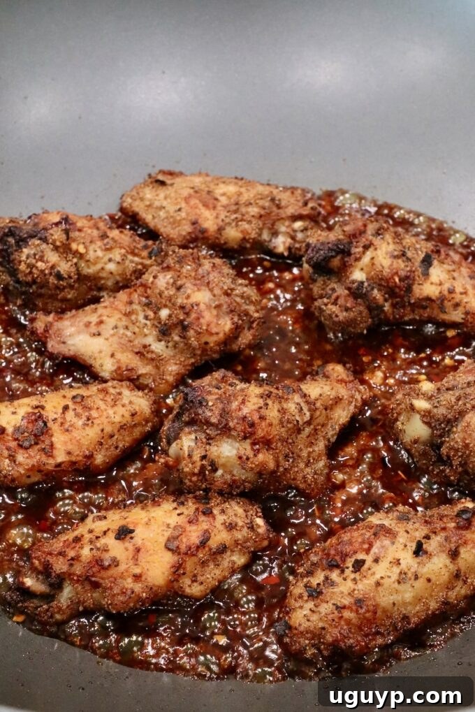 Cooked chicken wings being tossed in the General Tso sauce in a wok on the stove